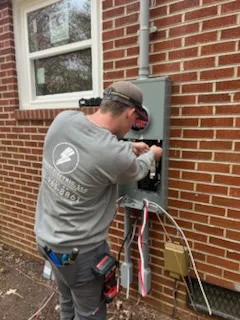 A worker attending to open electrical service equipment mounted on a brick house wall