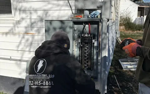 Workers beside an open exterior electrical service panel at a home.